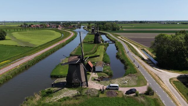 Aerial view of historic wooden windmills lining a tranquil canal in the dutch countryside, with lush green fields and a clear blue sky creating a famous and idyllic european landscape