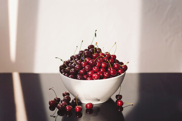 Fresh cherries glisten in a white bowl, capturing the light in a cozy kitchen setting © Cristina