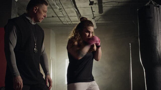Caucasian middle aged male coach correcting punching technique of Caucasian young female boxer in gym. Ideal for fitness center promotions and personal training advertisements