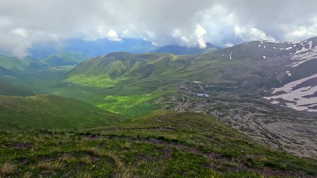 Clouds moving across Roshka Valley reveal green ridges and lingering snow in the Georgian Caucasus, documenting alpine weather, seasonal transition and remote geography for environmental travel media.