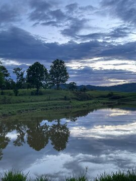 Peaceful countryside lake reflecting trees and dramatic evening sky in a tranquil natural landscape.