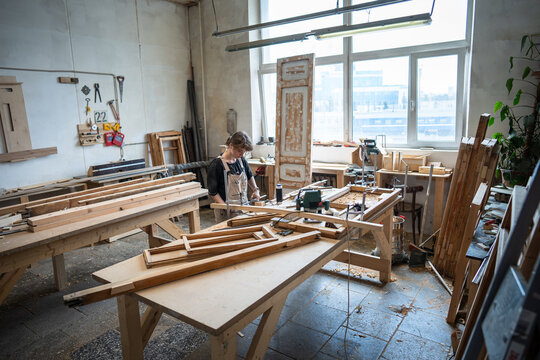 Craftsmanship and furniture restoration in small business woodshop focused woman works at workbench, female carpenter in spacious repair studio renovating wooden frame using tools and instruments.