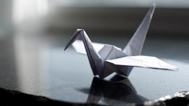 Paper origami crane model gracefully positioned on a reflective surface, showcasing intricate folds and details in a softly lit indoor environment