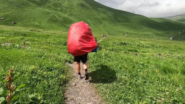 Tourist hiking toward Roshka with a covered backpack follows a narrow trail across Georgia's highland meadows, representing long-distance trekking, expedition logistics and remote destination tourism