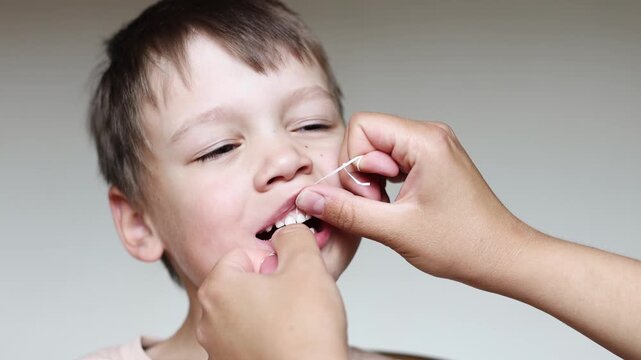 Mother cleans boy teeth with dental floss in slow motion. Close up shows gentle oral hygiene routine and healthy family dental care.