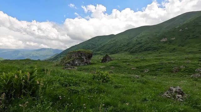 Clouds drifting above Roshka highlands cast changing shadows across green slopes and rocky pasture in Georgia, illustrating mountain weather, seasonal ecology and remote land conservation