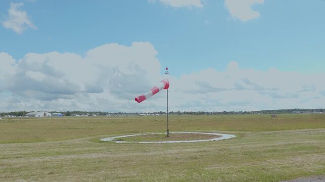 Windsock indicating wind direction on airfield runway under cloudy sky