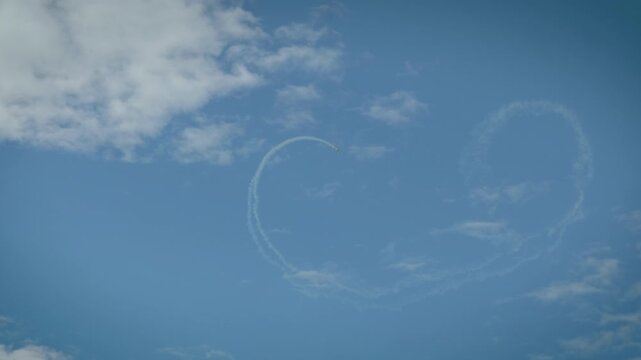 Precision aerobatic aircraft complete a perfect loop with contrails over white clouds.