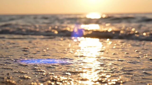 Sunlight reflects off gentle ocean waves washing onto sandy beach, creating a serene coastal scene during golden hour with shimmering water and soft textures