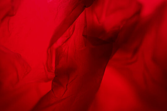 Extreme close up of red plastic texture background. The plastic surface is wrinkly and tattered making abstract pattern. Selective focus, shallow depth of field.