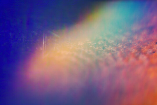 Extreme close up of abstract vibrant iridescent holographic rainbow foil background with lens flare. Glitter surface. Selective soft focus, shallow depth of field.