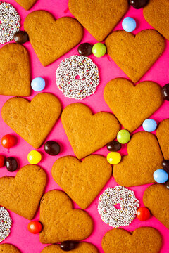 Top view of candies and heart shaped cookies on a vibrant pink background. Dessert photography, sweet treats.
