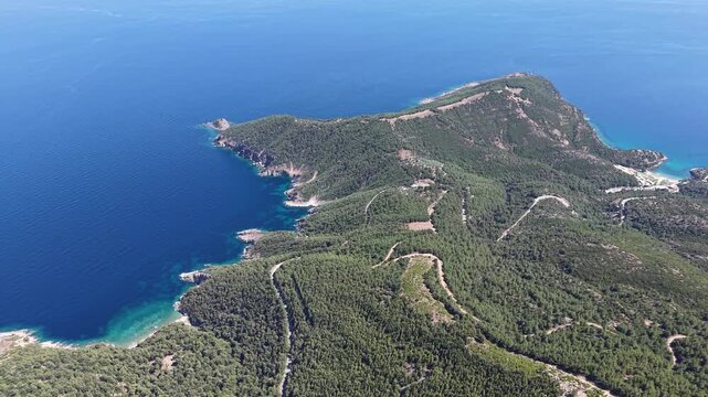 Wide aerial footage drifting above a rugged wooded peninsula bordered by turquoise coves and deep blue sea.