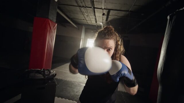 POV shot of young Caucasian woman boxing and throwing punches at camera in gym. Video suitable for female empowerment campaigns, fitness marketing, or mental health promotions