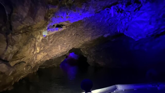 Tourists riding a boat through the underground canal of Prometheus Cave in Georgia, exploring illuminated limestone chambers during a guided subterranean excursion for travel and tourism content