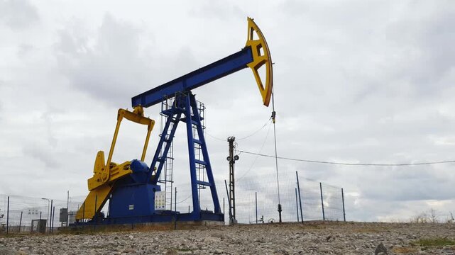 Oil pump jack machinery in an industrial landscape under cloudy sky