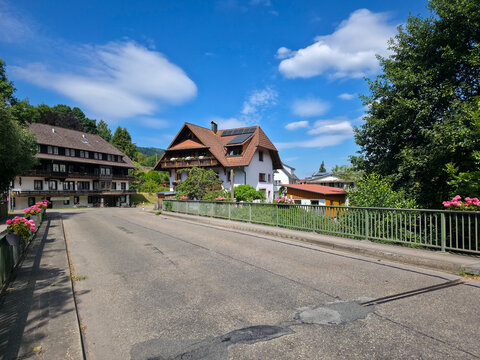 germany, traditional main street crossing charming bridge into picturesque simonswald village lined with historic black forest houses beneath radiant summer sky
