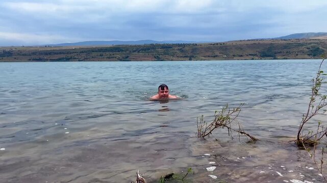 A tourist swims through the open water of Tbilisi Sea in Georgia, using the urban reservoir for endurance exercise and outdoor recovery, with distant hills supporting regional recreation