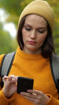 Attractive female tourist with a backpack using her mobile phone for navigation or communication during a hike in the picturesque autumn woods, staying connected with technology in nature