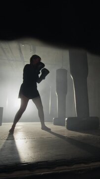 Vertical video of young woman practicing kickboxing, punching and kicking heavy bag in gym. Footage is perfect for fitness brand promos and gym advertisements
