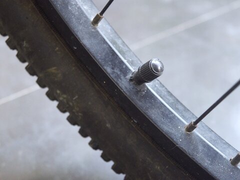 Close-up view of a black plastic valve cap on a bicycle wheel rim, highlighting the tire valve stem mechanism and tread texture