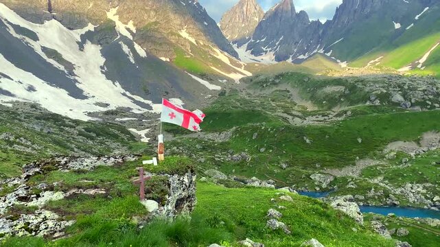 The Georgian flag waves above Abudelauri Lakes with Mount Chaukhi rising behind it, connecting national identity with alpine tourism, regional heritage, trekking culture, destination branding