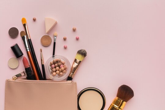 Assorted makeup tools and brushes on soft pink backdrop.