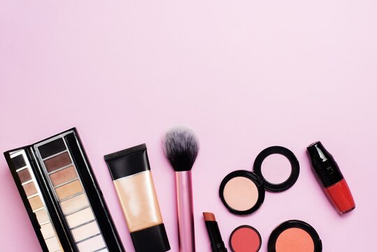 Colorful makeup collection arranged on pink background.