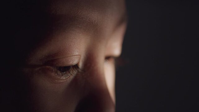 Close-up side view of a young boy's brown eye illuminated by soft light, with the eye open, glistening, and gazing forward, capturing human emotion, vision, and facial detail.