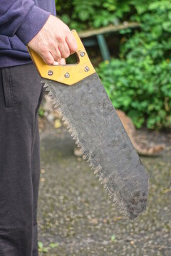 A hand in a glove holds a one metal hacksaw with a yellow handle against a green background in the street