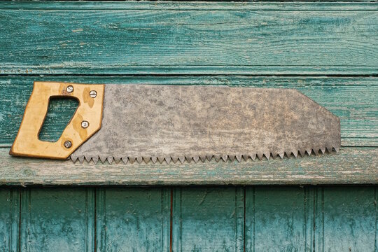 one old iron gray hacksaw with a yellow wooden handle lies on a green table