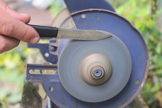 One male worker holds a knife in his hands and sharpens the iron blade on a grinding wheel on an electric sharpening machine on a table