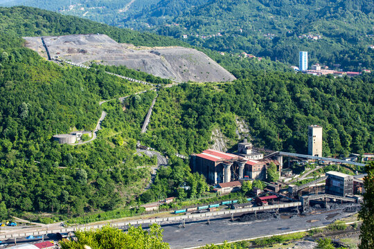 An aerial view of an industrial coal mining and processing facility nestled within a lush green forest landscape.