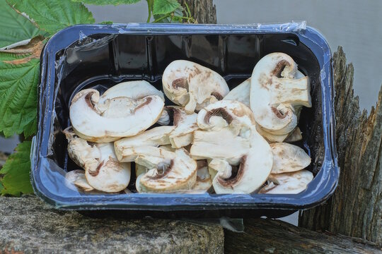 A pile of sliced ​​white fresh champignon mushrooms in a black box on a brown table in the street