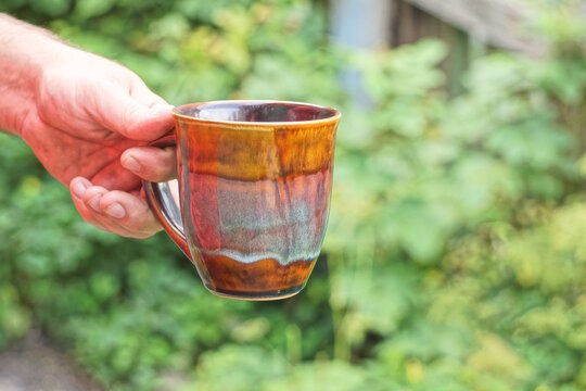 hand holding one big brown ceramic cup on green background in the street