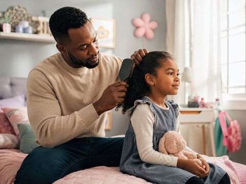 A tender father-daughter moment unfolds as a man gently grooms his daughter's dark curly hair in a cozy bedroom setting, filled with soft lighting and a pink floral theme.