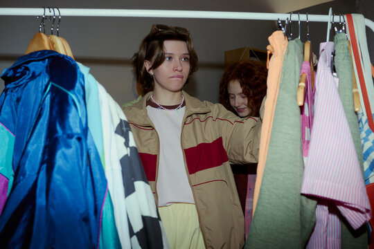 Young girls browsing clothing rack and choosing outfits in resale shop, expressing sustainable fashion shopping and youth consumer behavior. Ideal for thrift retail marketing and style content