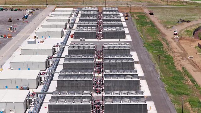 Large air-cooled dry coolers and fluid cooling units at a high-tech data center at daytime, showcasing industrial scale and modern infrastructure aerial tilt down flyover