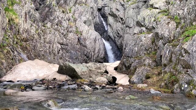 Snowmelt cascades through a narrow rock gorge near Juta in Georgia, feeding a cold mountain stream beside lingering snow and illustrating seasonal runoff, freshwater resources, and alpine hydrology