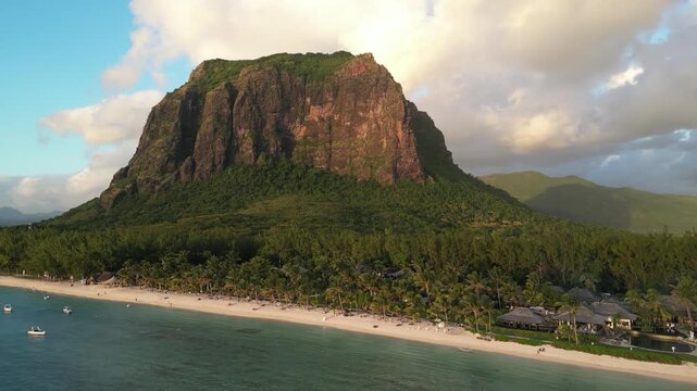 Aerial drone perspective of the Le Morne Brabant monolith rising over the tropical coastline of Mauritius. Lush volcanic peak overlooking the sandy beach and clear coastal water