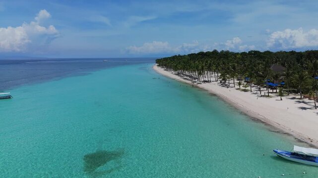 Aerial ascends and pans right to reveal Dumaluan Beach, clear turquoise water, white sand, palm trees, and boat in Panglao