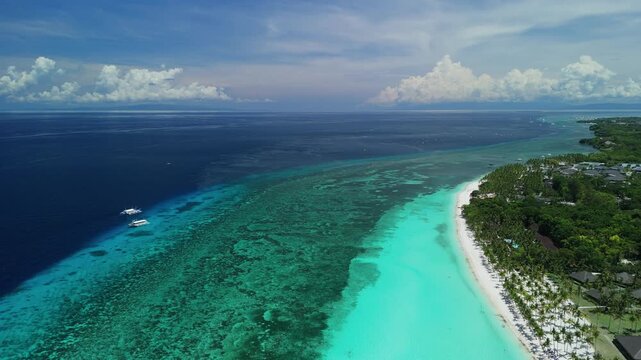 Drone pulls back over Dumaluan Beach, showing reef flats, white sand, boats, resorts, and the Panglao coastline