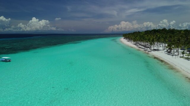 Drone ascends, pans right, and pulls back over Dumaluan Beach, showing reef flats, white sand, boats, and Panglao coastline