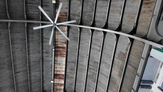 Ceiling fan spinning inside a public railway station with large metal roof structure industrial beams and transportation infrastructure in daylight.