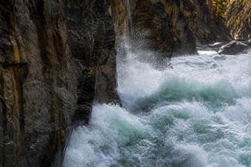 River torrent crashing against canyon rock wall with white foam. © Steve