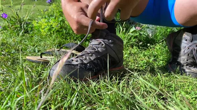 A hiker tightens the laces on rugged trekking boots in a grassy Georgian campsite, preparing footwear for secure traction, ankle support, route safety, endurance, and a demanding day in the Caucasus.