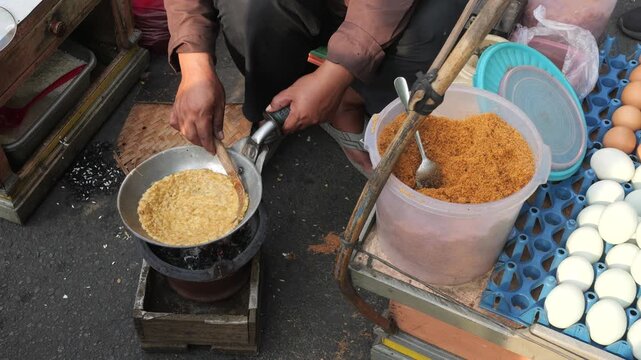 A partially cooked mixture of glutinous rice and duck eggs is heated in a pan and continuously fanned during the preparation of Kerak Telor to bind the eggs and the rice into a cohesive mixture,