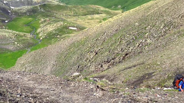 Mountaineer ascending Chaukhi Pass climbs a steep scree slope with a loaded backpack in Georgia, presenting physical endurance, route difficulty and demanding highland expedition conditions.
