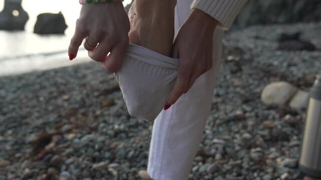 Woman putting on sock before walking on pebble beach ready for travel and adventure.