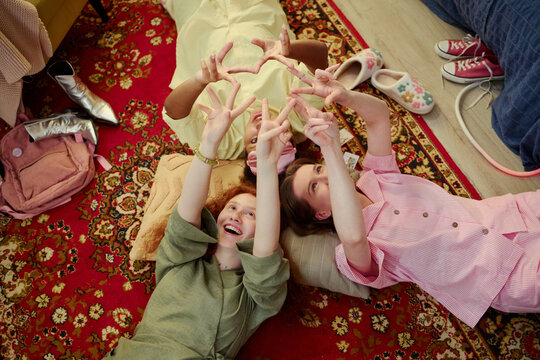 Overhead view of diverse young women lying on floor and forming heart and star shapes with hands, expressing friendship and inclusion. Ideal for community, youth lifestyle, social campaign use